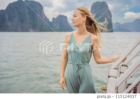 Attractive woman in a dress is traveling by boat in Halong Bay. Vietnam. Travel to Asia, happiness emotion, summer holiday concept. Picturesque sea landscape. Ha Long Bay, Vietnam Attractive woman in a dress is traveling by boat in Halong Bay. Vietnam. Travel to Asia, happiness emotion, summer holiday concept. Picturesque sea landscape. Ha Long Bay, Vietnam 115124037
