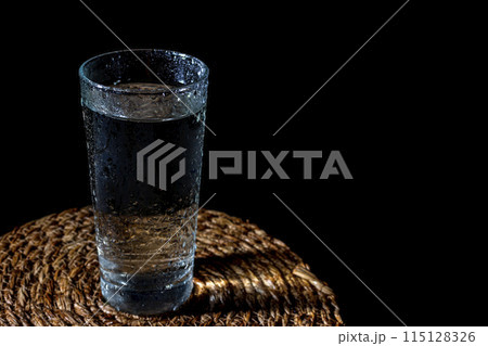 a misted glass of clean water on a wicker stand on a black background 115128326