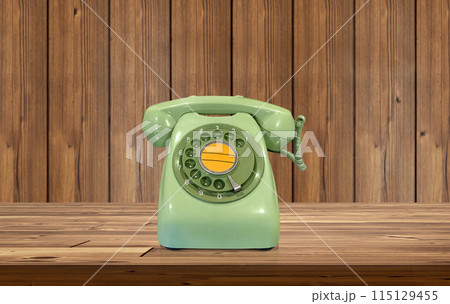 Old fashioned green desk phone on wooden table There is a wooden wall behind it. 115129455