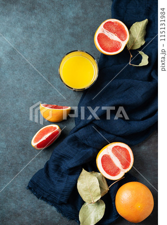 juicy red grapefruit, glass of juice and slices on a blue background with a dark napkin. juicy red grapefruit, glass of juice and slices on a blue background with a dark napkin. 115131984