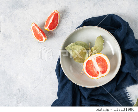juicy red grapefruit in a plate and slices on a blue background with a dark napkin. juicy red grapefruit in a plate and slices on a blue background with a dark napkin. 115131990