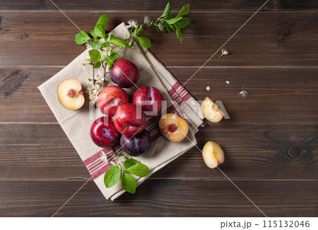 a few juicy red plums with branch blossom flowers on a napkin on a brown wood background. a few juicy red plums with branch blossom flowers on a napkin on a brown wood background. 115132046
