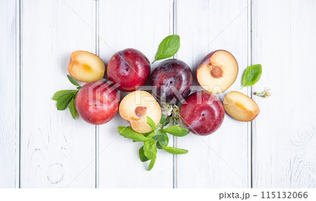 Concept flat lay with  juicy red plums and green leaves  on a white  wood background. Top view 115132066