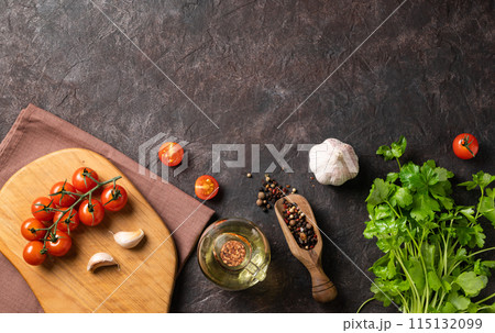 Spices and fresh herbs parsley, garlic, pepper, tomatoes and oil on a dark brown background.  115132099
