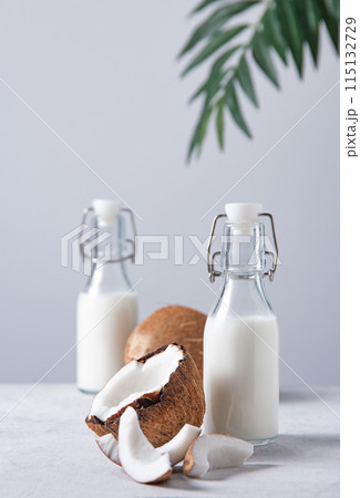 Two  vegan milk bottles on white marble table with half coconuts and palm branch. Front view 115132729