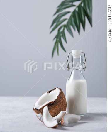 Healthy vegan milk bottle on white marble table with half coconuts and palm branch.  115132732
