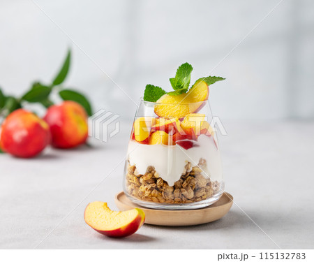 Greek yogurt parfait with peach and granola in a glass on a light background Greek yogurt parfait with peach and granola in a glass on a light background 115132783