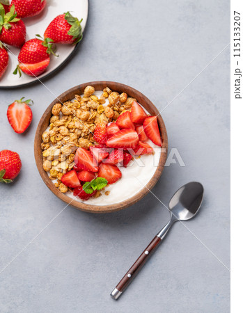 Natural yogurt with granola and strawberries in a wooden bowl on a blue background  115133207