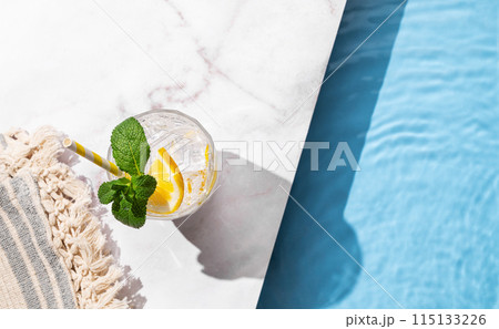 Cold lemonade in a glass with lemon, mint and ice on a marble background with the edge of a pool. Cold lemonade in a glass with lemon, mint and ice on a marble background with the edge of a pool. 115133226