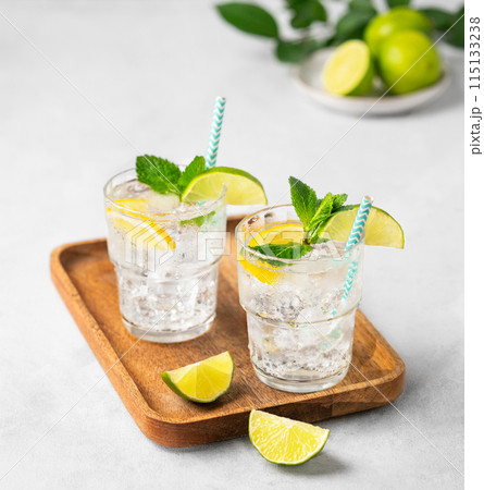 Two glasses of mojito cocktail or tonic with lemon, lime, mint and ice on a wooden board. Two glasses of mojito cocktail or tonic with lemon, lime, mint and ice on a wooden board. 115133238