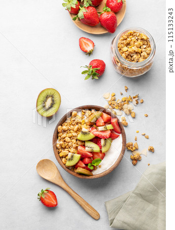 Natural yogurt with granola, kiwi and strawberries in a wooden bowl on a light background  115133243