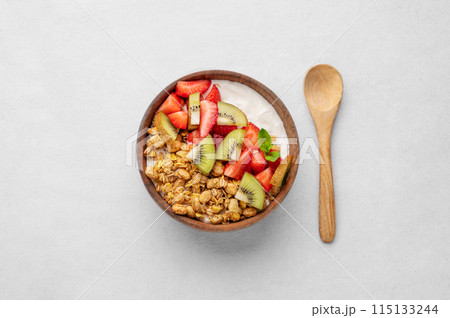 Natural yogurt with granola, kiwi and strawberries in a wooden bowl on a light background with spoon 115133244