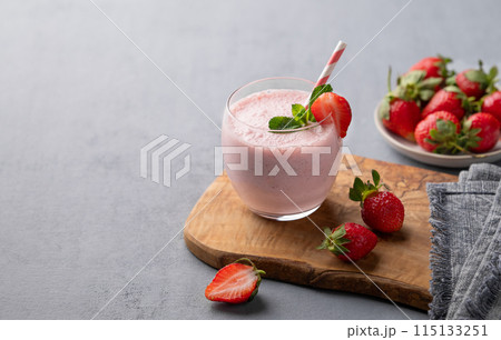 A glass of fresh strawberry smoothie with mint on a wooden board on a blue background with berries. 115133251