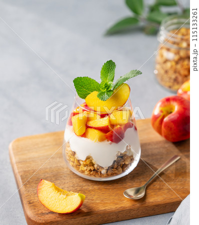 Greek yogurt parfait with peach and granola in a glass on a wooden board on a light background  115133261