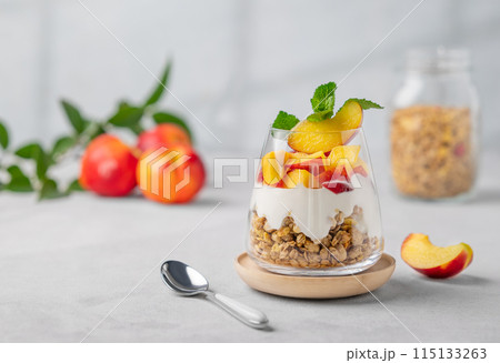Greek yogurt parfait with peach and granola in a glass on a light background with fresh fruits 115133263