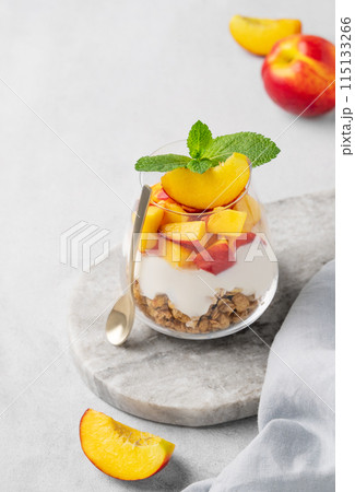 Greek yogurt parfait with peach and muesli in a glass on a marble board on a light background Greek yogurt parfait with peach and muesli in a glass on a marble board on a light background 115133266