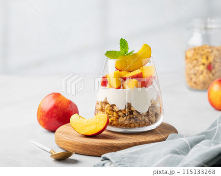 Greek yogurt parfait with peach and muesli in a glass on a wooden board on a light background 115133268