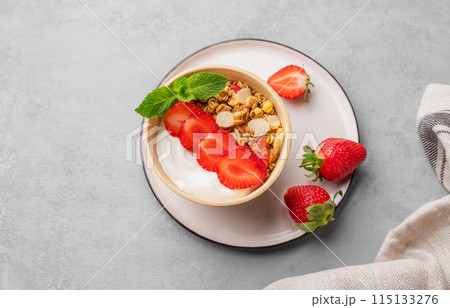 Natural yogurt with muesli and strawberries in a bowl on a blue background with fresh berries 115133276