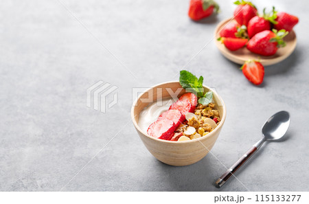Natural greek yogurt with granola and strawberries in a bowl on a blue background with fresh berries 115133277