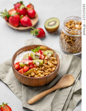 Natural yogurt with granola, kiwi and strawberries in a wooden bowl on a light background  115133285