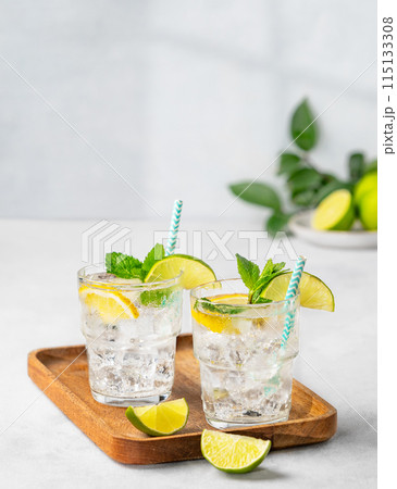 Two glasses of mojito cocktail or tonic with lemon, lime, mint and ice on a wooden board. Two glasses of mojito cocktail or tonic with lemon, lime, mint and ice on a wooden board. 115133308