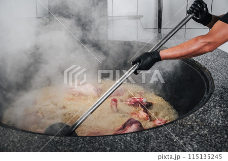 male chef cooks meat in boiling cauldron for traditional oriental Uzbek pilaf in kitchen of restaurant in Uzbekistan male chef cooks meat in boiling cauldron for traditional oriental Uzbek pilaf in kitchen of restaurant in Uzbekistan 115135245
