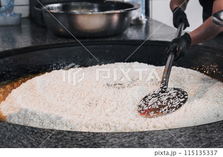 hands of a male cook cooking traditional oriental Uzbek rice pilaf in a cauldron. Central Asian Pilaf Center in Uzbekistan 115135337