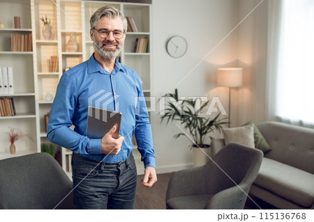 Man psychologist wearing blue shirt holding clipboard standing in his office 115136768
