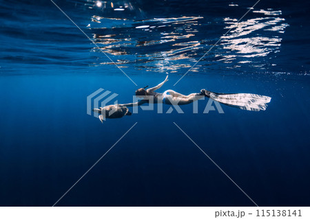 Woman snorkeling underwater and touching turtle in blue sea. Woman snorkeling underwater and touching turtle in blue sea. 115138141