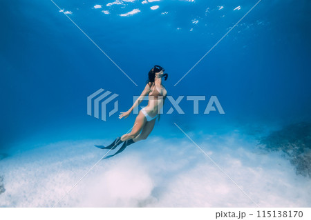 Female free diver swims underwater over sandy sea in blue ocean. 115138170