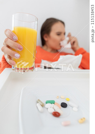 A teenager sitting on the bed snot his nose before taking the next dose of tablet medicine. 115138453