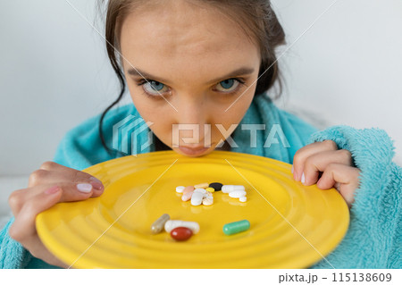 In front of the young girl's nose lies a plate with vitamins and tablets necessary to swallow to fight the disease. In front of the young girl's nose lies a plate with vitamins and tablets necessary to swallow to fight the disease. 115138609