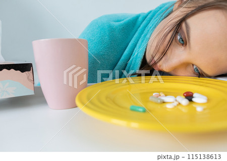 In front of the young girl's nose lies a plate with vitamins and tablets necessary to swallow to fight the disease. In front of the young girl's nose lies a plate with vitamins and tablets necessary to swallow to fight the disease. 115138613