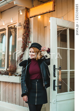 Brunette woman in black leather jacket and black hat standing outside 115138885
