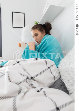 A young teenager drinks hot tea with herbs while lying on her bed under the covers. A young teenager drinks hot tea with herbs while lying on her bed under the covers. 115139152
