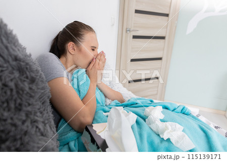 A teenager coughing strongly, cutting her mouth with her hand, lying in her bed under a warm blanket. 115139171