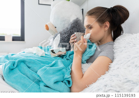 A cold teenager snot tears his nose in a handkerchief all the time under a warm duvet. 115139193