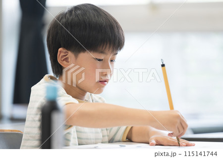 明るい小学校の教室で習字を教わる小学生の男の子 115141744