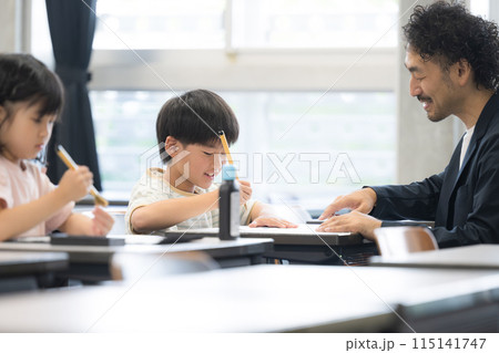 明るい小学校の教室で習字を教わる小学生の男の子 115141747