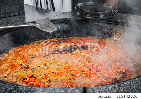 carrots, chickpeas and raisins are boiled in a cauldron to cook traditional Uzbek pilaf in the kitchen of a restaurant in Tashkent, Uzbekistan 115142626