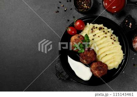 Fried cutlets with mashed potatoes, tomatoes and herbs. Black plate on a black background 115143461