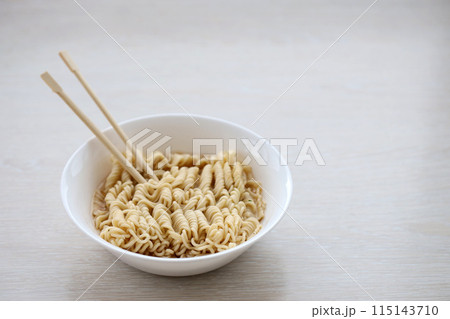 Bowl of instant cooking noodles with wooden chopsticks on white wooden table close up Bowl of instant cooking noodles with wooden chopsticks on white wooden table close up 115143710