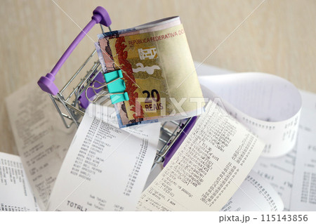 Brazilian reais money bills bunch in shopping trolley surrounded by many paper receipts close up 115143856