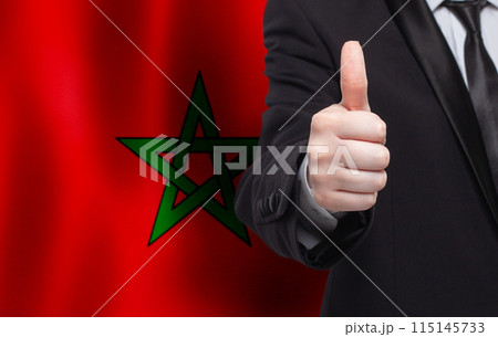 Maroccan concept. Businessman showing thumb up on the background of flag of Marocco Maroccan concept. Businessman showing thumb up on the background of flag of Marocco 115145733