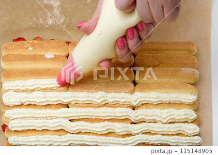Women's hands cover rows of savoiardi with cream using a pastry bag. Women's hands cover rows of savoiardi with cream using a pastry bag. 115148905