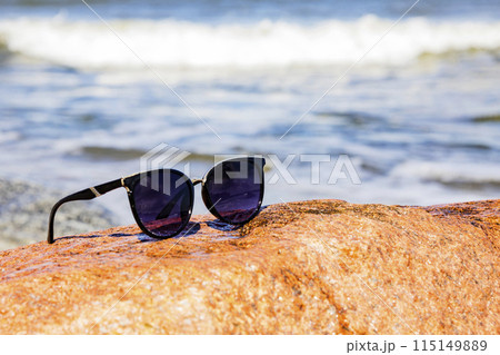 A pair of stylish sunglasses placed on a rocky surface close to the ocean A pair of stylish sunglasses placed on a rocky surface close to the ocean 115149889