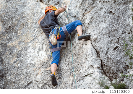 Close up of a climber with equipment on a belt, climbing a rock wall 115150300