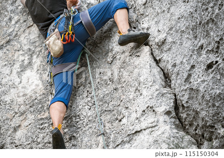 Close up of a climber with equipment on a belt, climbing a rock wall Close up of a climber with equipment on a belt, climbing a rock wall 115150304