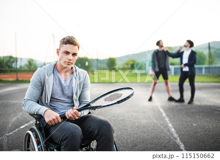 Disabled young man in a wheelchair playing tennis with his friends. Teamwork and male friendship. Disabled young man in a wheelchair playing tennis with his friends. Teamwork and male friendship. 115150662