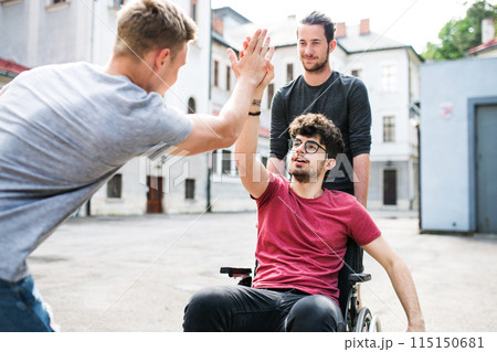 Young man in wheelchair spending free time outdoor with friends, having fun in city. Male friendship. 115150681